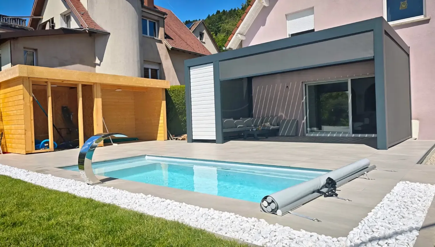 Installation d'une piscine coque à Grendelbruch, Haut-Rhin, sur terrain en pente. Aménagement d'une terrasse de 70m², cabanon extérieur et pergola.