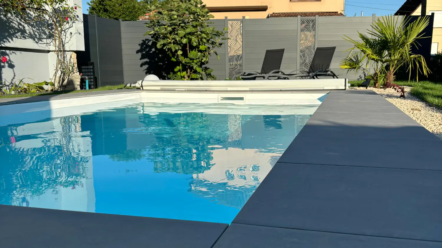 Piscine en béton construite sur mesure avec plage immergée et jet d'eau, margelles en pierre et pergola en bois.
