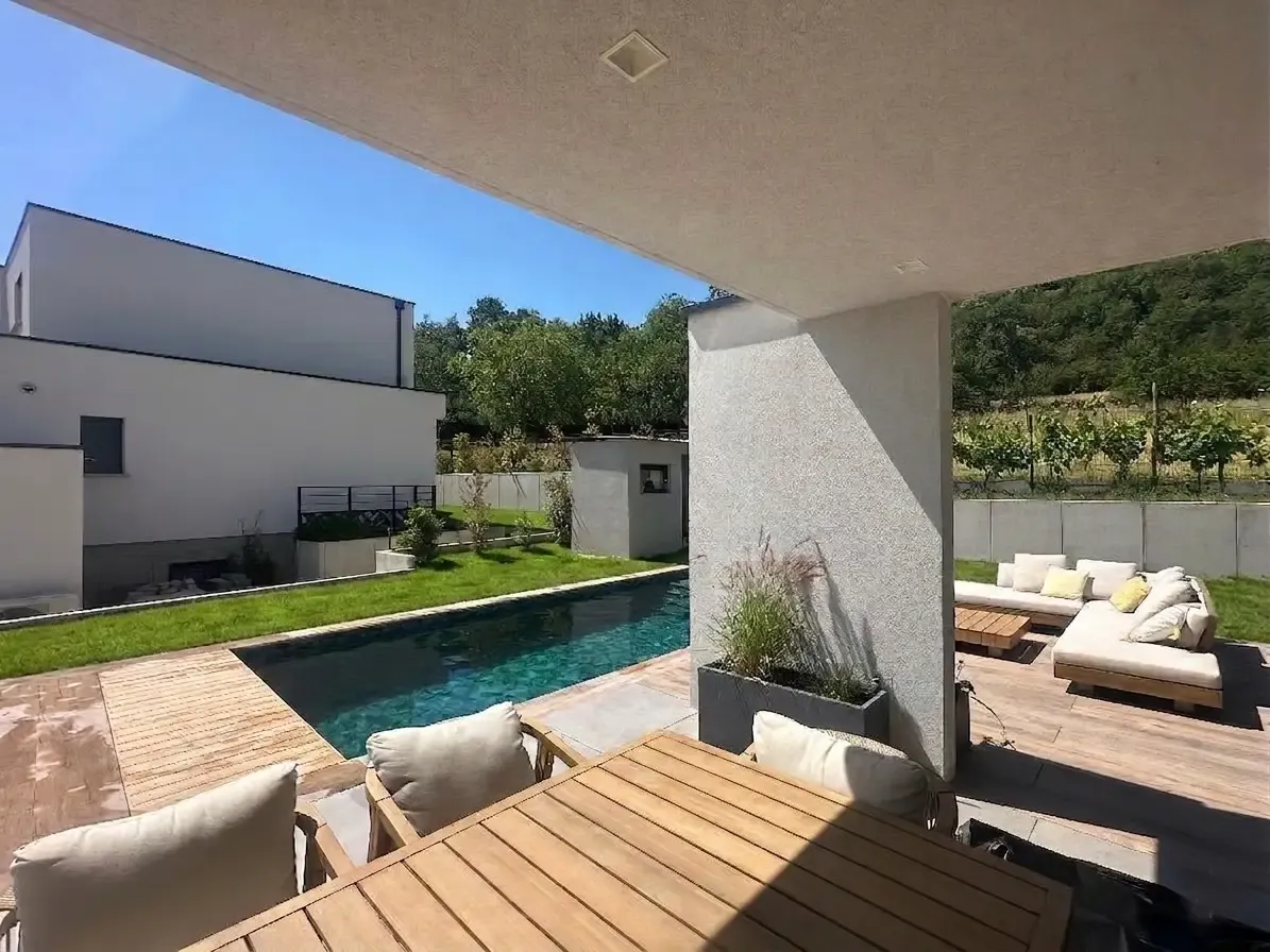 Piscine et pelouse vues depuis la terrasse couverte de la maison