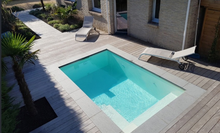 Piscine coque avec margelles en pierre et habillage de terrasse en bois.