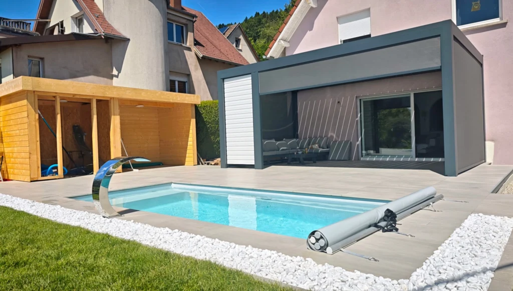 Installation d'une piscine coque à Grendelbruch, Haut-Rhin, sur terrain en pente. Aménagement d'une terrasse de 70m², cabanon extérieur et pergola.