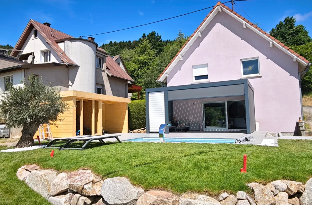 Installation d'une piscine coque à Grendelbruch, Haut-Rhin, sur terrain en pente. Aménagement d'une terrasse de 70m², cabanon extérieur et pergola.